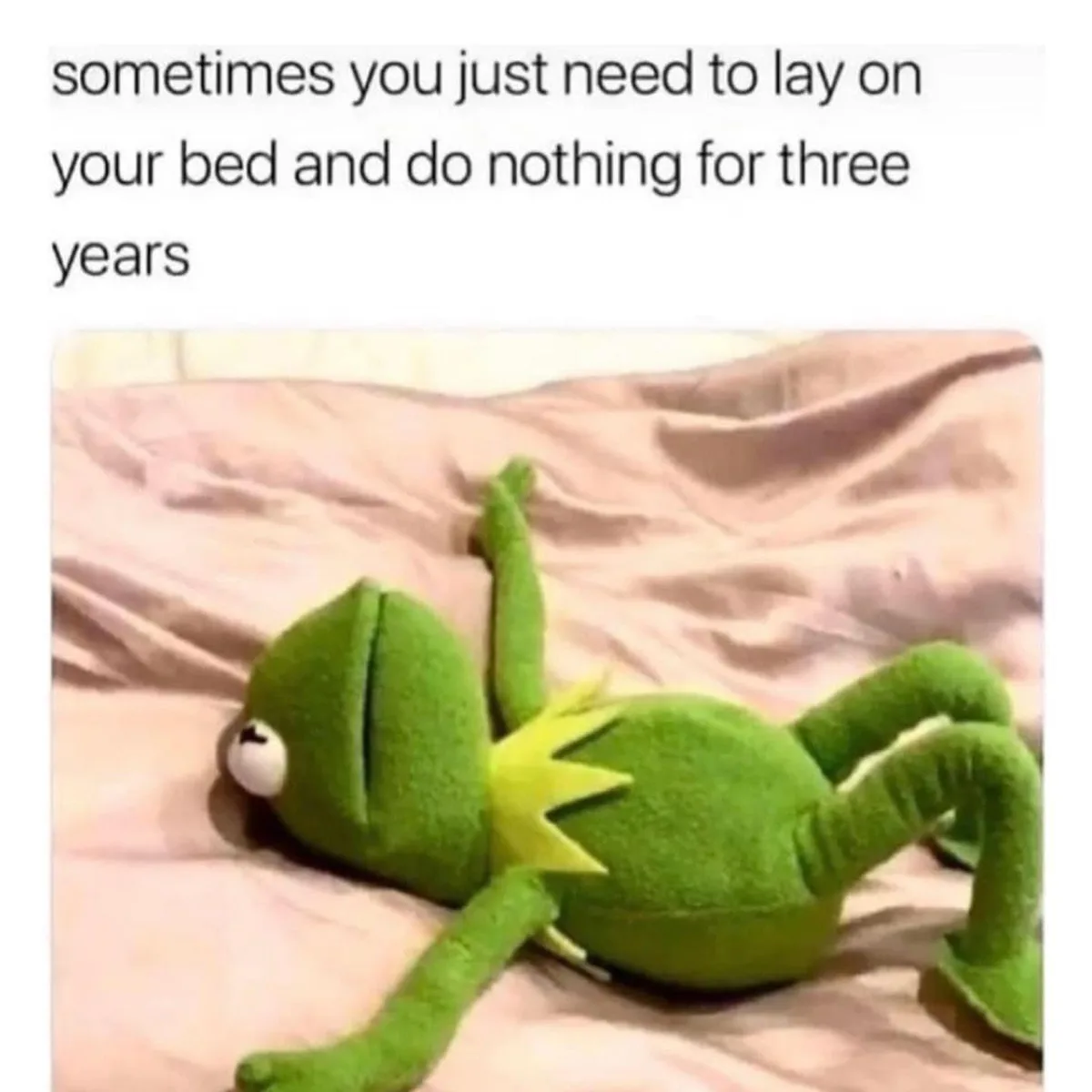 A green plush frog toy, resembling Kermit the Frog, lies sprawled on its back on a rumpled pink bedsheet, limbs splayed out…