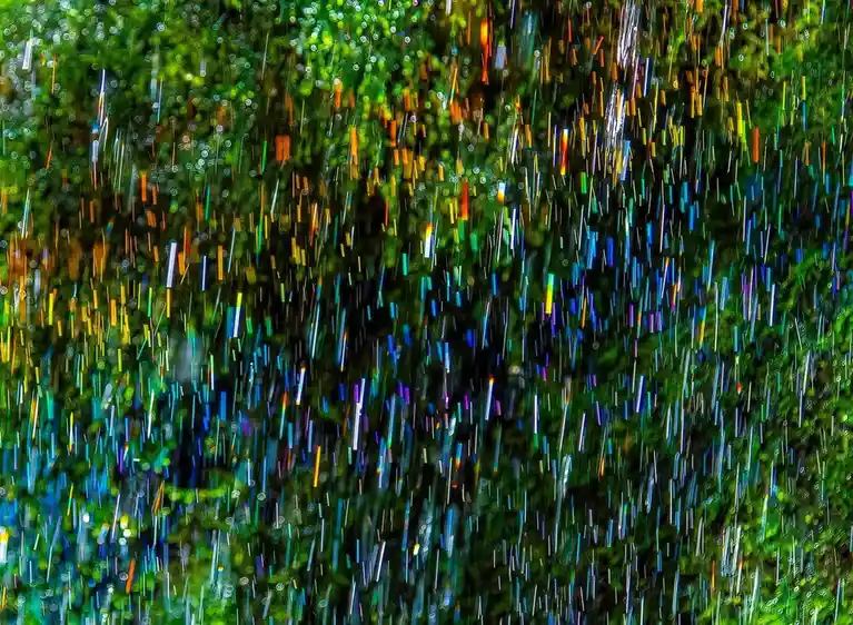 An abstract image of vibrant, multicolored streaks resembling falling rain against a blurred green background, overlaid with…