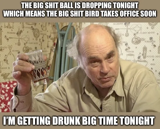 An older man with a balding head and receding hairline, wearing a beige button-up shirt, holds a small glass with a dark…