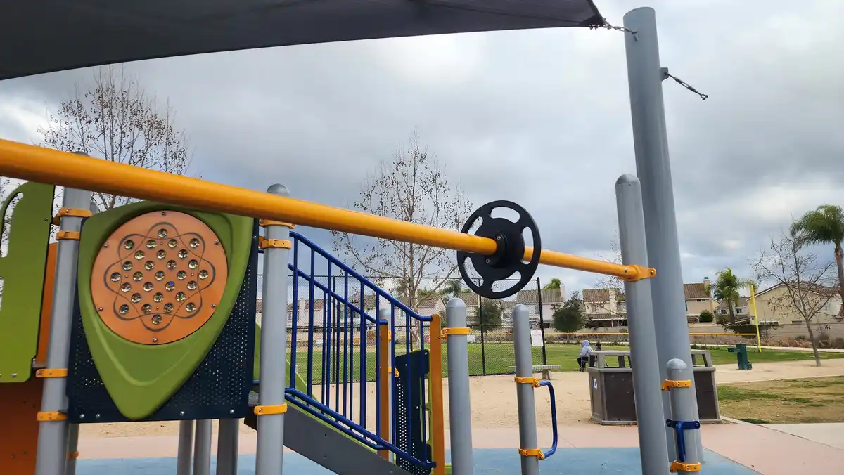 a photo of a colorful playground structure under a cloudy sky, featuring a yellow bar with a black weight plate attached…