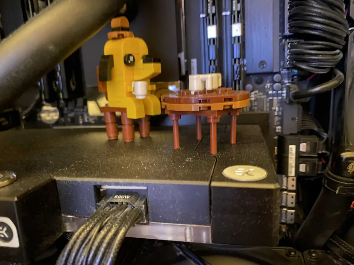 A yellow Lego figure resembling Pac-Man stands on a server rack, holding a white coffee cup, next to a small Lego table with…