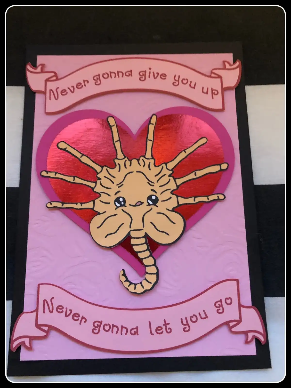 A handmade pink Valentine's card features a cute, cartoonish spider with an elephant's trunk and face, set against a shiny…