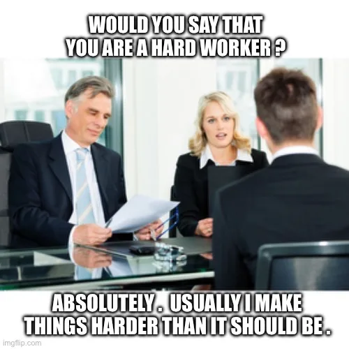 A man in a suit sits across a glass desk from another man during what appears to be an interview, while a woman in a suit…