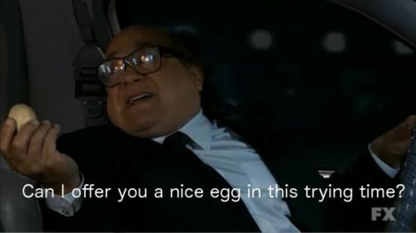 A man in a suit and glasses sits in a car, holding an egg in his left hand while gesturing with his right. The overlaid text…
