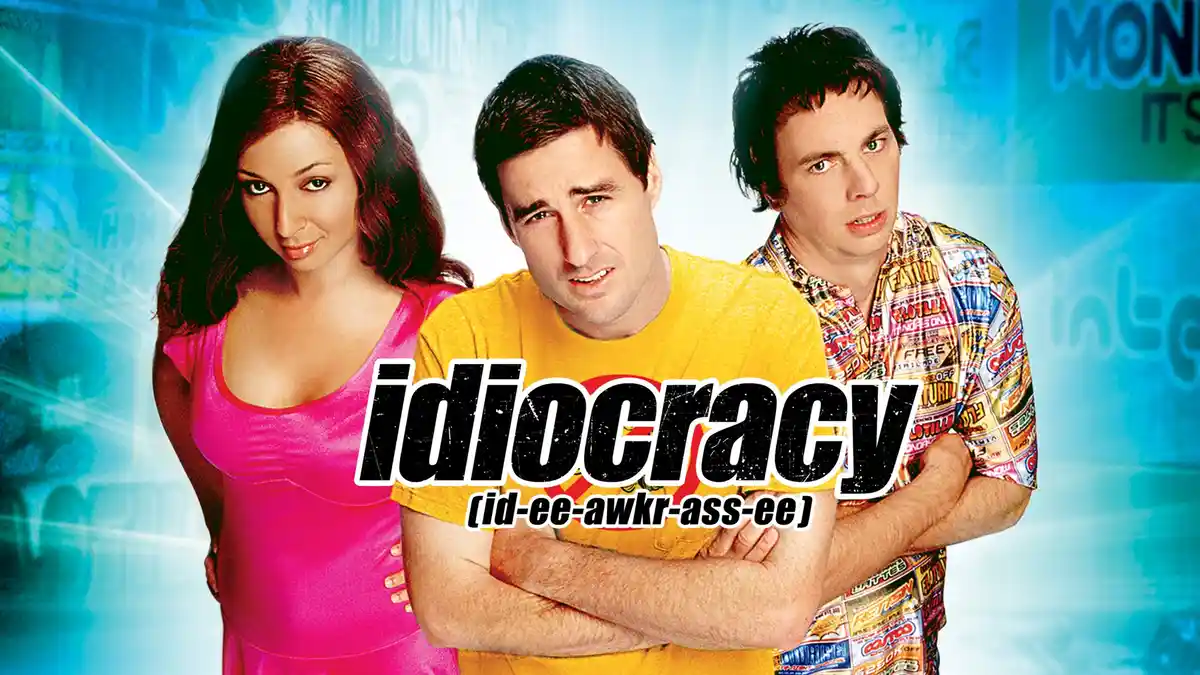 The image shows three people from the movie 'Idiocracy' against a blue, digitally blurred background. The central man in a…