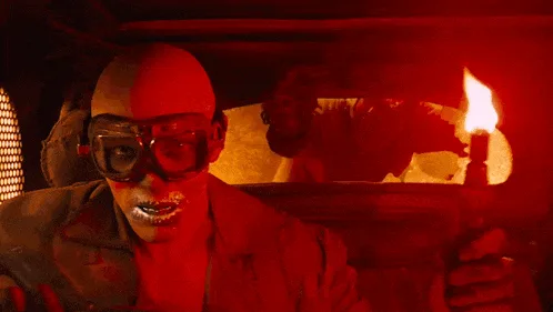 A six-panel image sequence from a movie showing a bald man with goggles and silver-painted teeth in a red-lit environment…