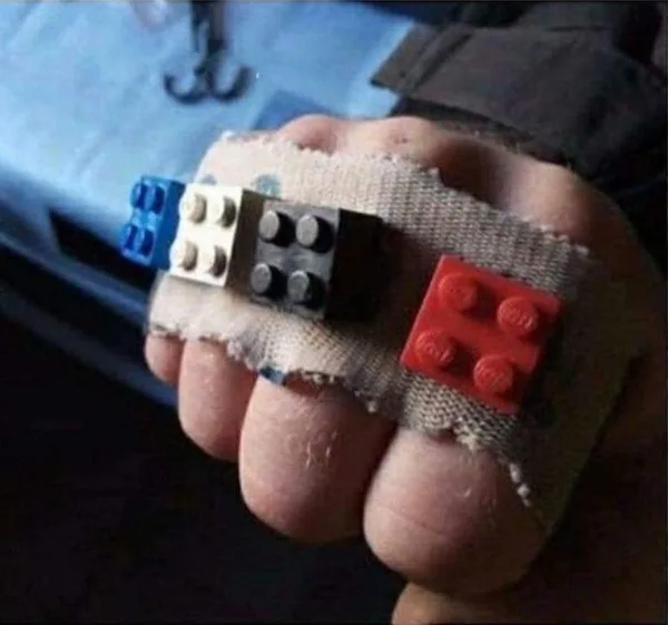 A close-up photo shows a child's hand wrapped in a torn beige bandage, with four Lego bricks (blue, white, black, and red)…