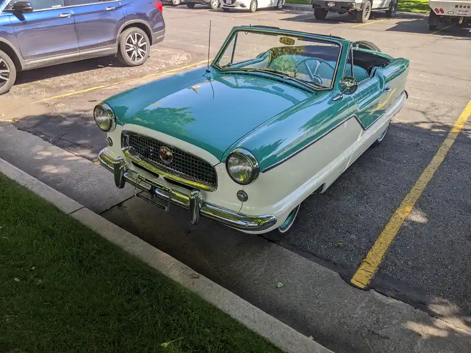 A vintage teal and cream two-tone convertible car with chrome accents is parked in a modern asphalt parking lot next to a…