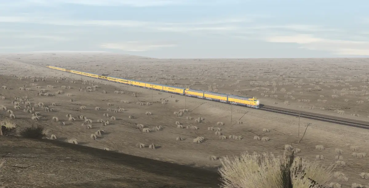 A long yellow train travels across a vast, arid desert landscape with sparse vegetation under a pale sky. The overlaid text…