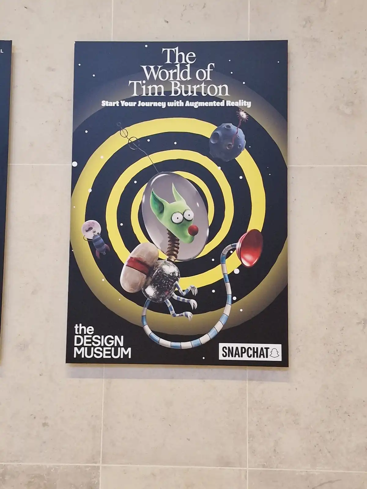 A promotional poster for 'The World of Tim Burton' exhibit at the Design Museum, featuring a cartoonish green alien-like…