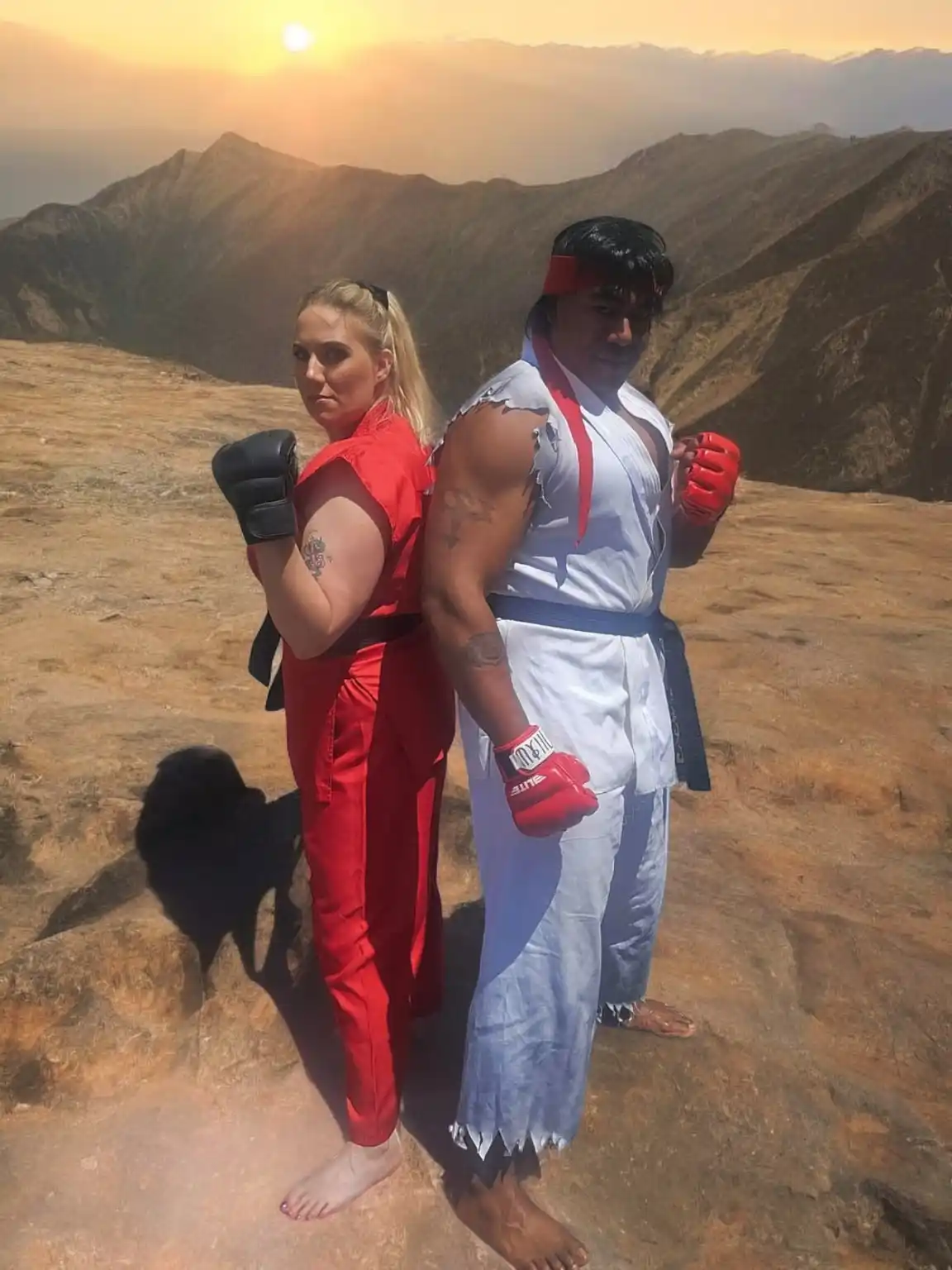 Two people dressed as Street Fighter characters, Chun-Li in red and Ryu in white, stand back-to-back on a rocky mountain…