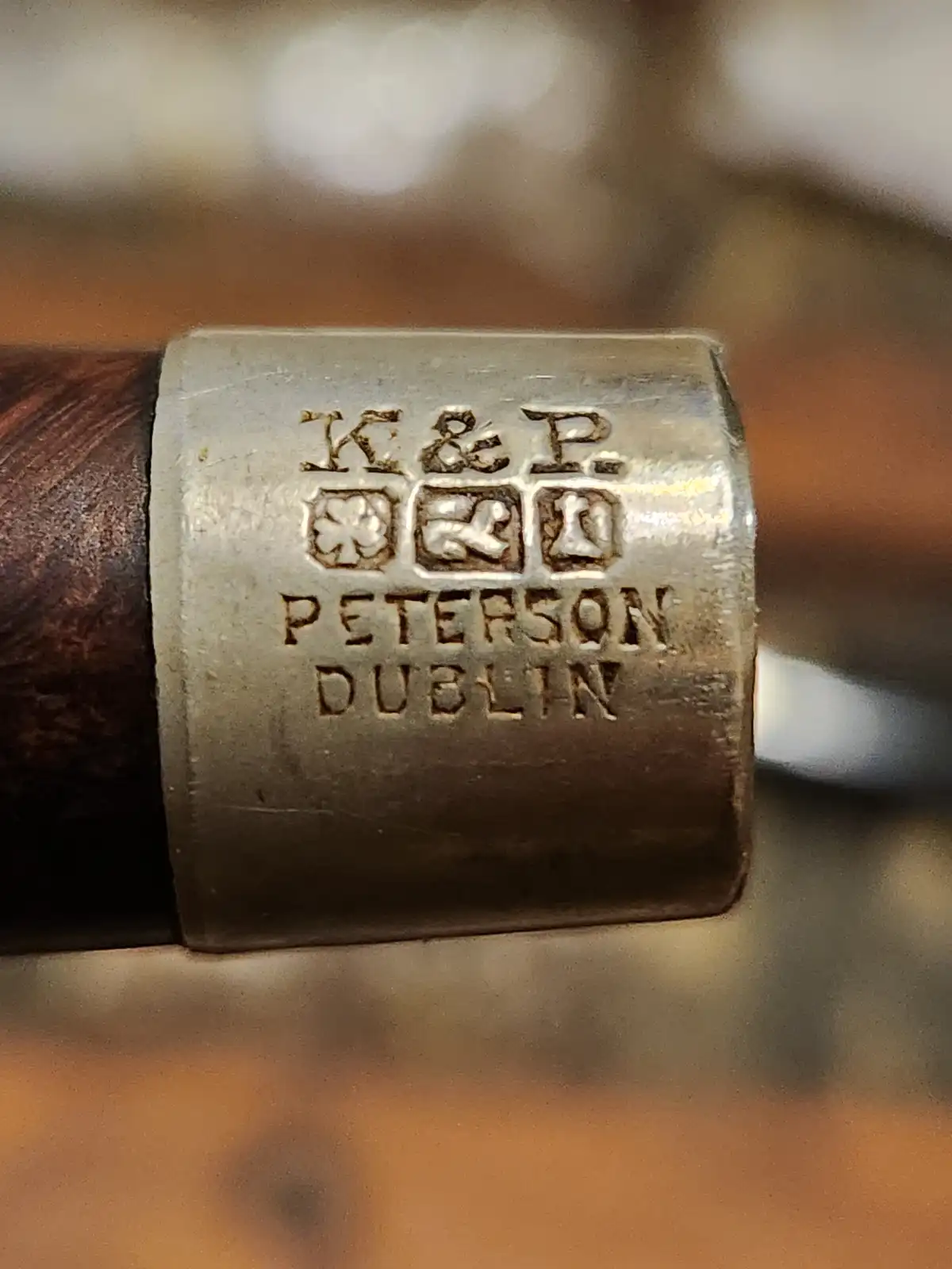 A close-up of a silver band on a wooden object, engraved with 'K & P', three small symbols (a shamrock, a stylized 'P', and…