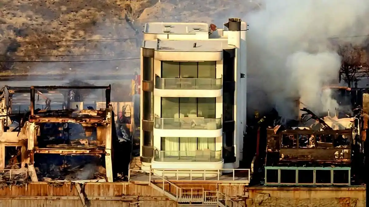 an aerial view shows a modern, multi-story glass building standing untouched amidst surrounding structures that are heavily…