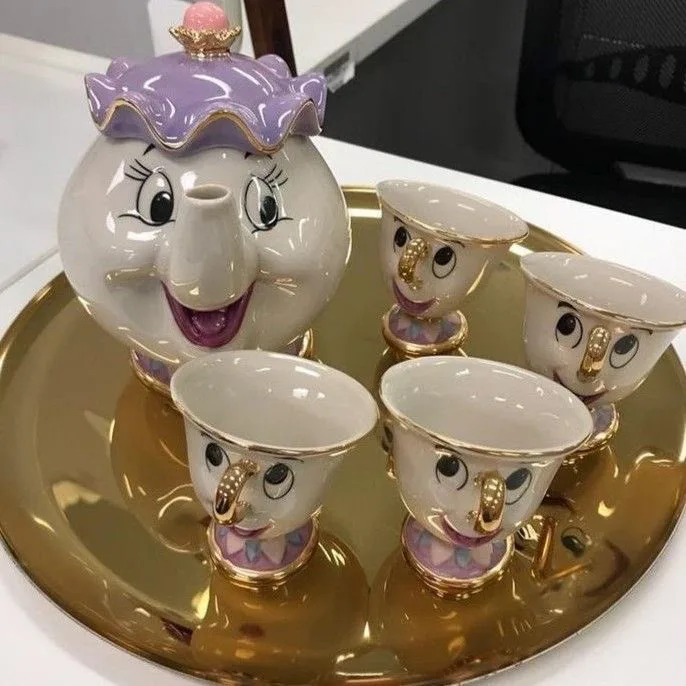 A ceramic tea set featuring characters from Beauty and the Beast, including Mrs. Potts the teapot with a purple crown and…