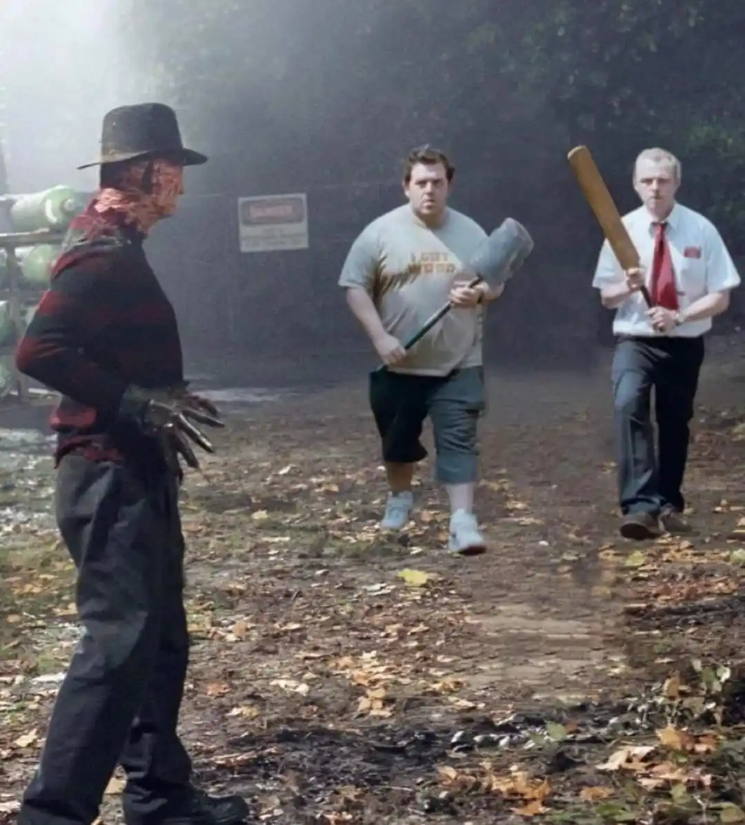 A still from a horror movie shows Freddy Krueger facing two men walking toward him; one wears a 'I GOT WOOD' t-shirt and…
