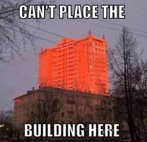 A tall, orange-lit apartment building is shown standing atop a shorter, older, grayish building. Bare tree branches frame…