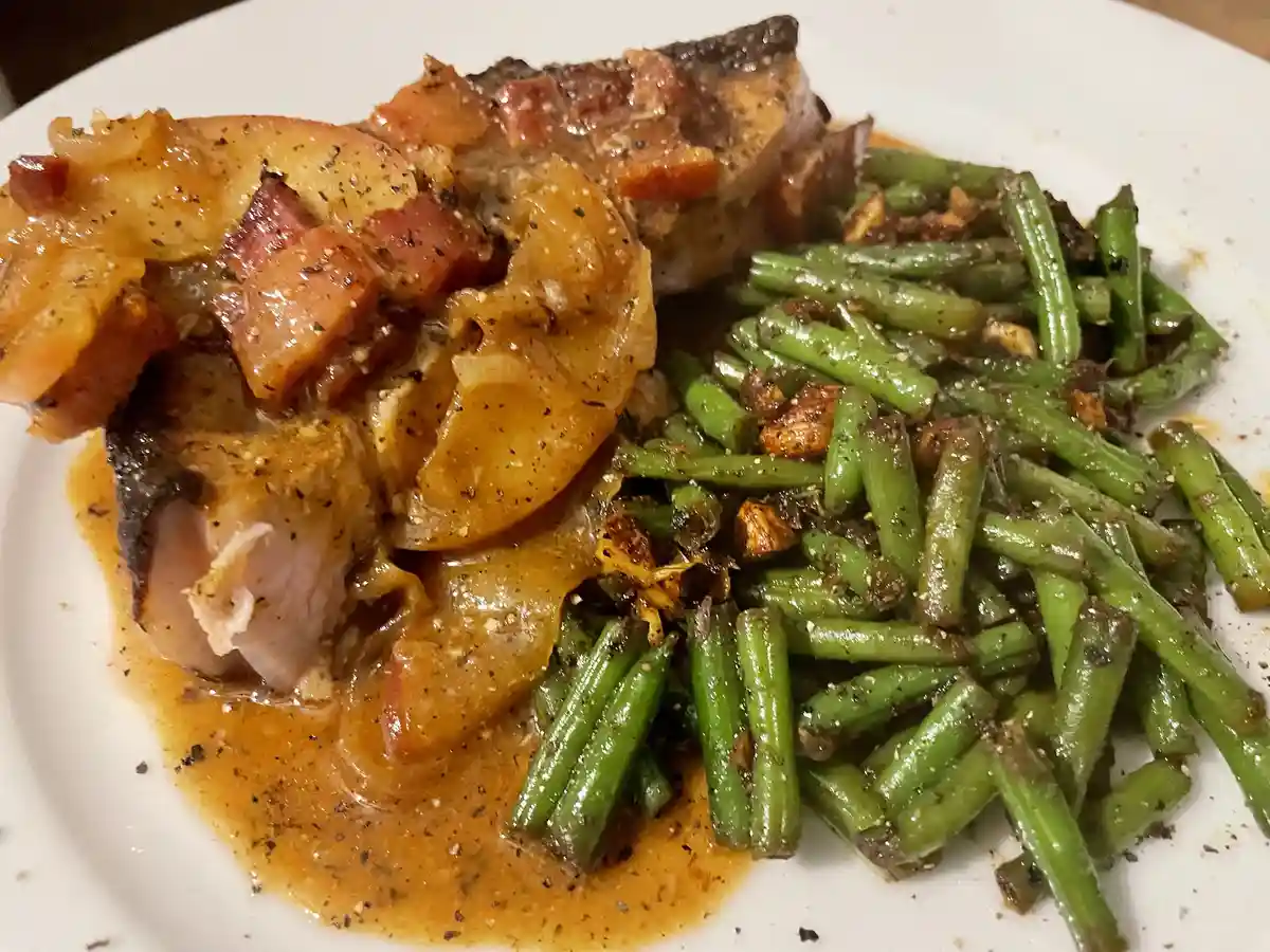 A close-up photo of a plated meal featuring a piece of meat covered in sauce and bacon bits, alongside a serving of green…