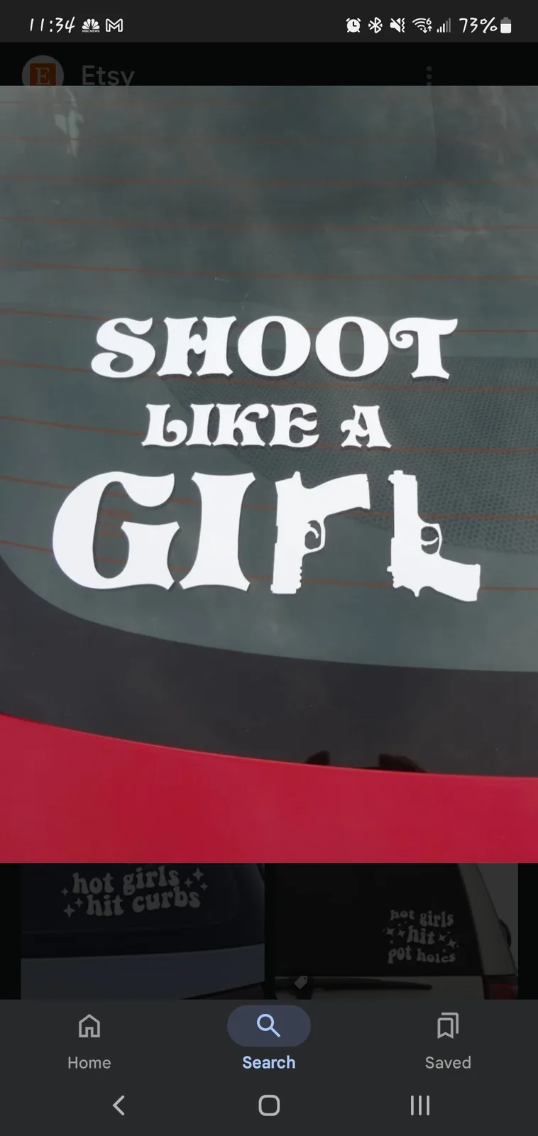 A white vinyl decal on a car's rear window reads 'SHOOT LIKE A GIRL', where the 'I' and 'L' in 'GIRL' are stylized as…