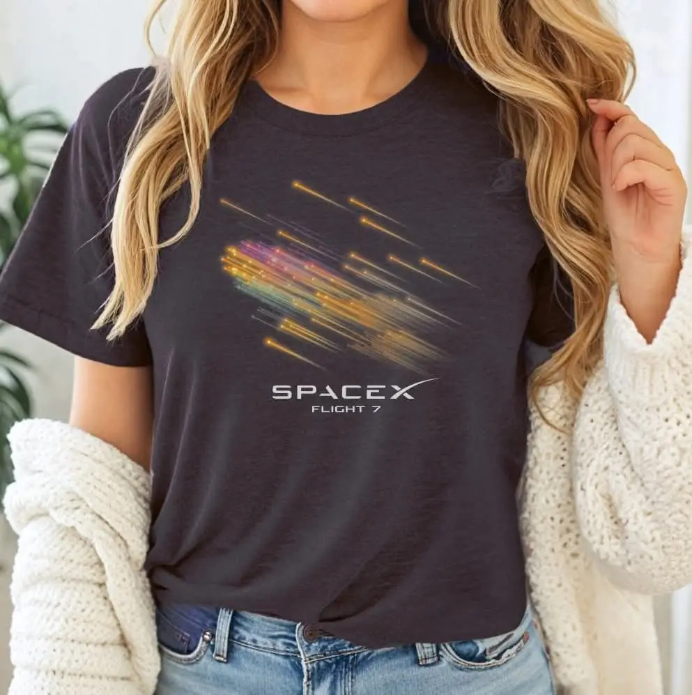 A person with long blonde hair wears a dark gray t-shirt featuring a colorful, streaky graphic resembling a rocket trail or…