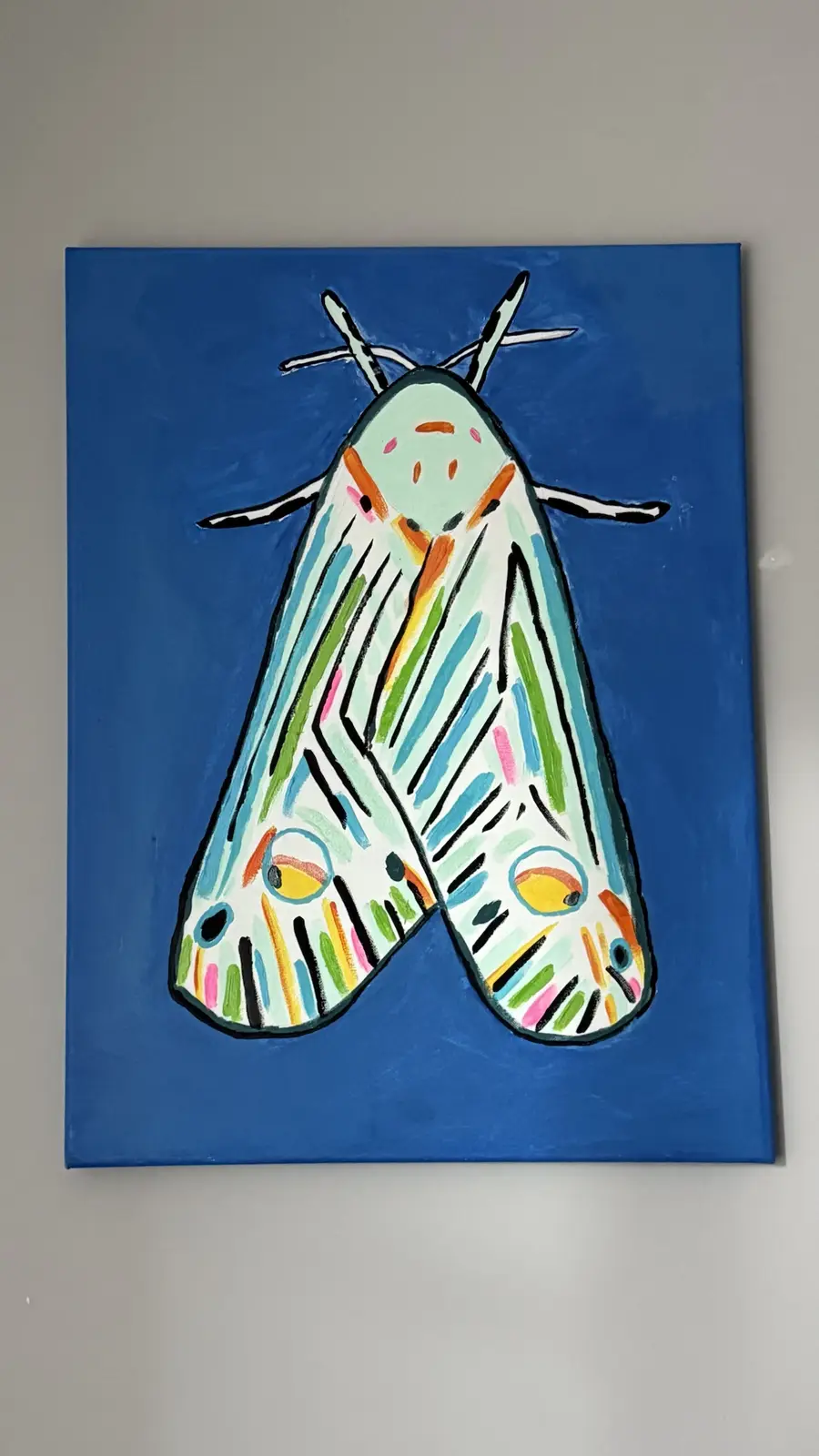 A colorful, stylized painting of a moth on a blue background, featuring vibrant stripes and patterns in green, blue, pink…