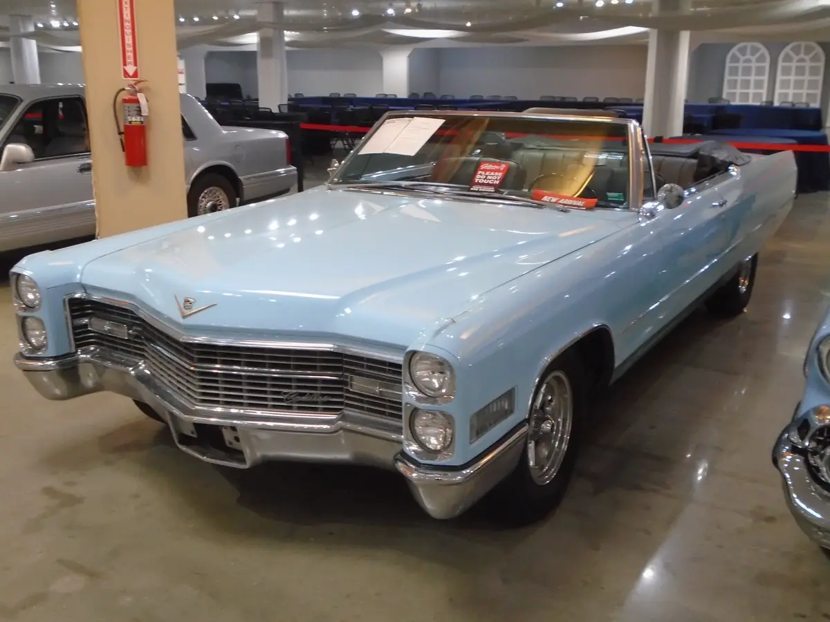 A light blue classic Cadillac convertible is displayed indoors, likely in a museum or showroom, with a red "PLEASE DO NOT…