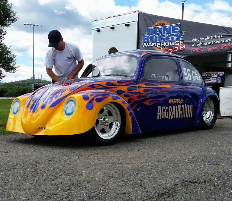 A heavily modified, low-slung blue and yellow Volkswagen Beetle race car with orange and blue flame decals and the text…