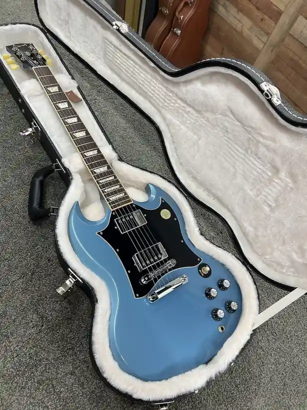 A light blue electric guitar with a black pickguard and chrome hardware rests inside an open, white-furred hardshell case on…