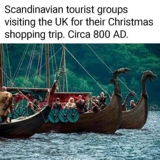 The image shows two Viking longships with dragon-head prows sailing on water, filled with people dressed in Viking-style…