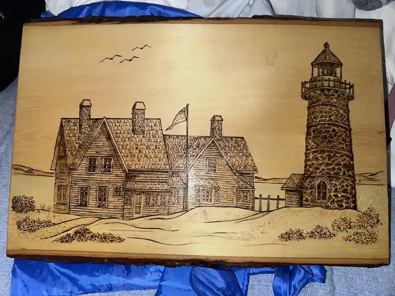 A wood-burned artwork depicts a large, detailed house with three chimneys and an American flag, standing beside a stone…