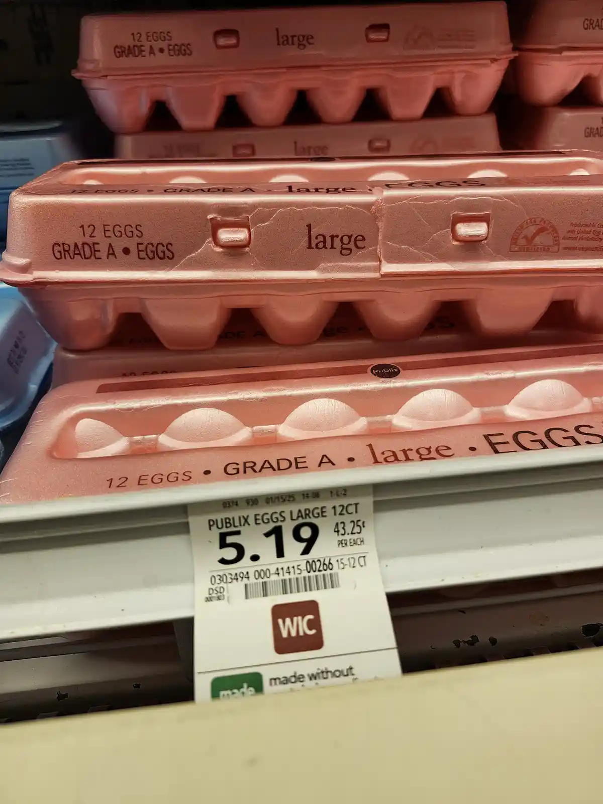 A close-up photo of stacked pink egg cartons labeled '12 EGGS GRADE A • large' on a grocery store shelf. A price tag below…