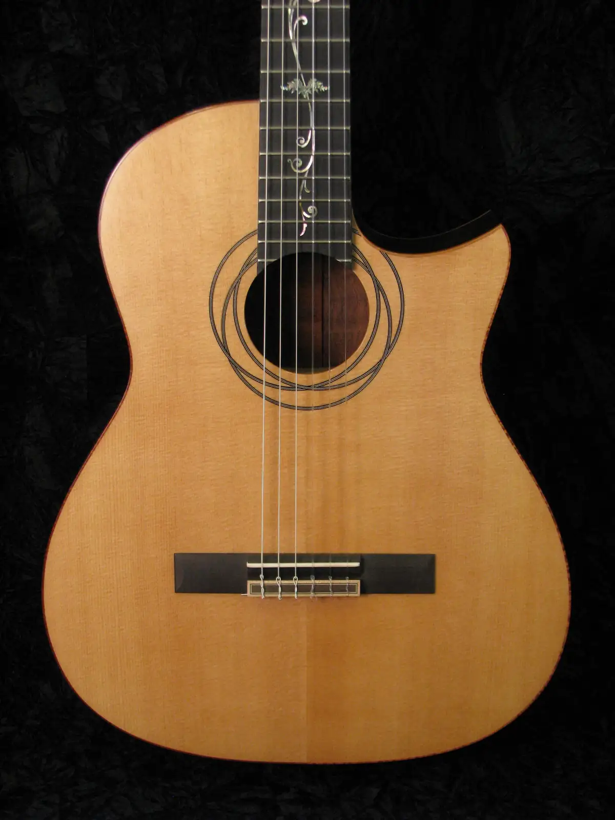A close-up photo of a light-wood acoustic guitar with a cutaway body, set against a black textured background. The guitar…