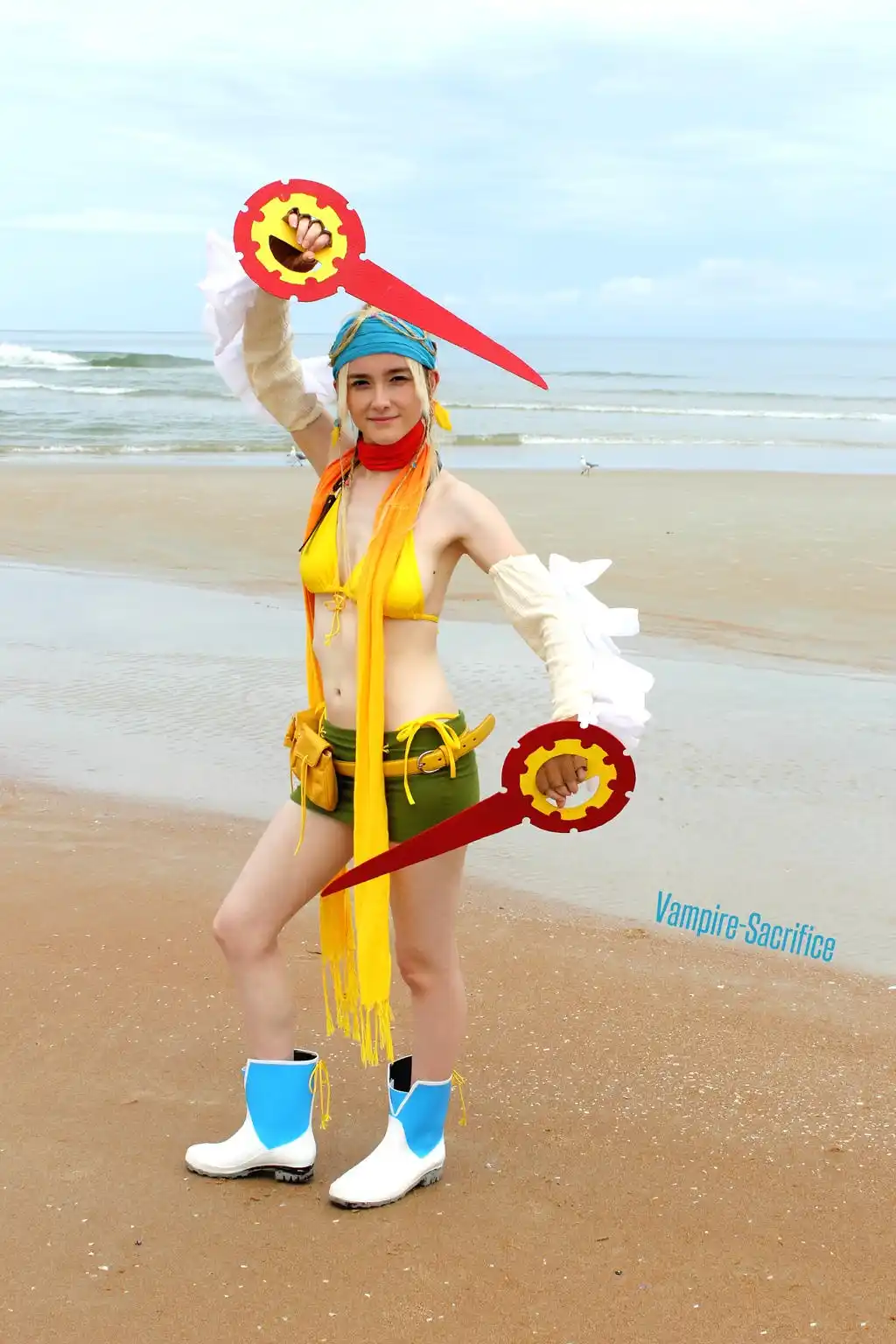 A person in a cosplay of a video game character stands on a beach holding two oversized red and yellow prop keys, one in…