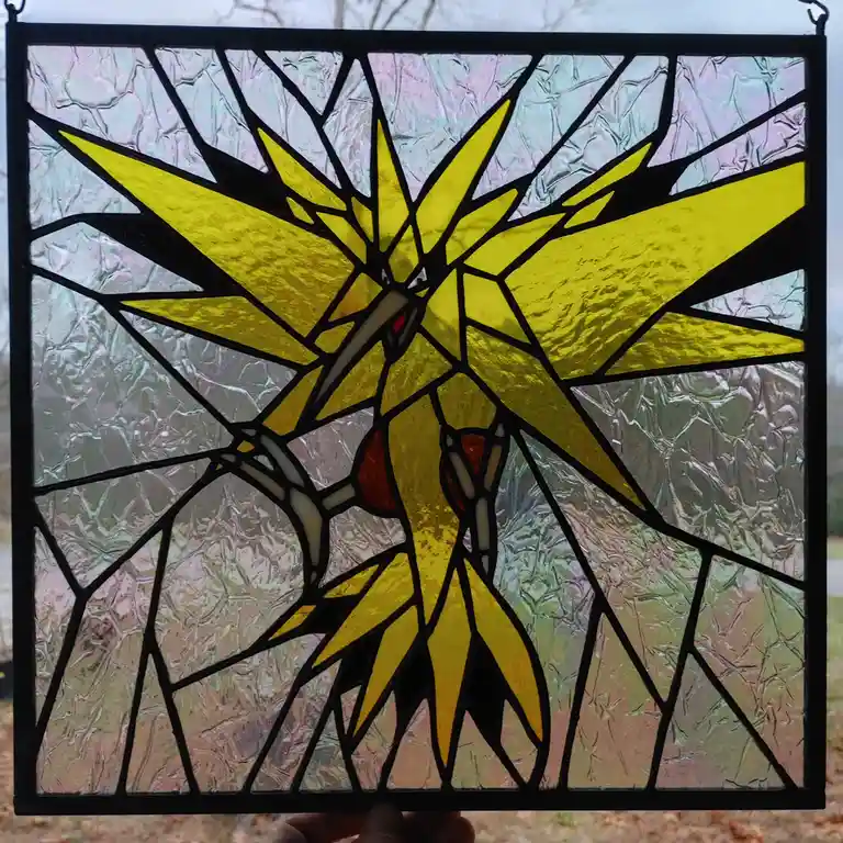 A person holds up a stained glass window depicting the Pokémon Solgaleo, rendered in yellow glass with black lead lines…