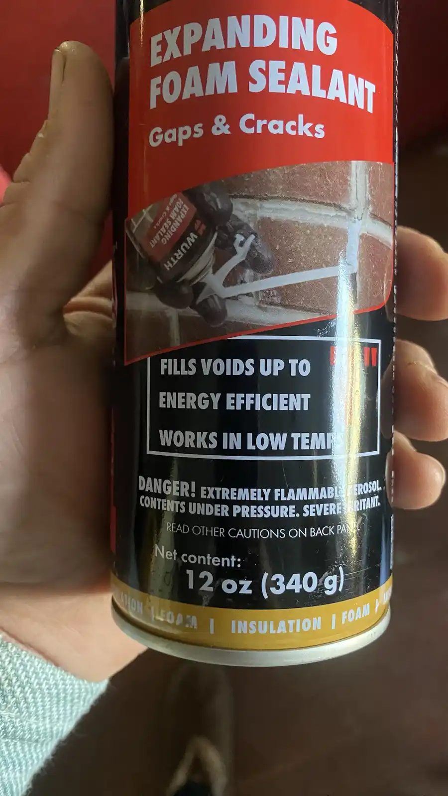 A hand holds a can of expanding foam sealant, showing its label which includes the text 'FILLS VOIDS UP TO ENERGY…