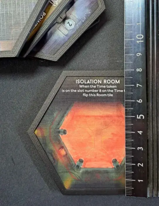 A close-up photo of a hexagonal game tile labeled 'ISOLATION ROOM' with instructions to flip it when a 'Time token' is on…