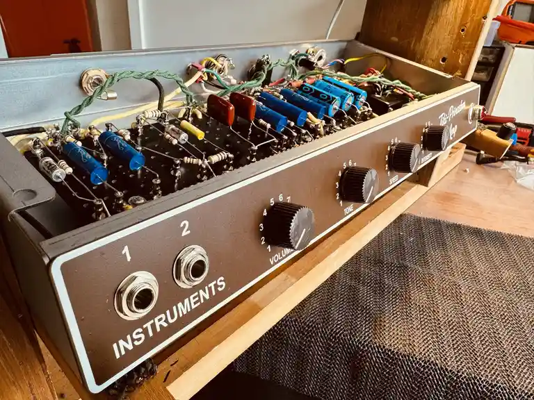 A close-up photo of a vintage-style guitar amplifier with its panel open, revealing a complex internal circuit board with…