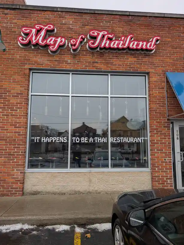 A brick building with a red neon sign reading 'Map of Thailand' above a large window. Inside the window, white text reads…