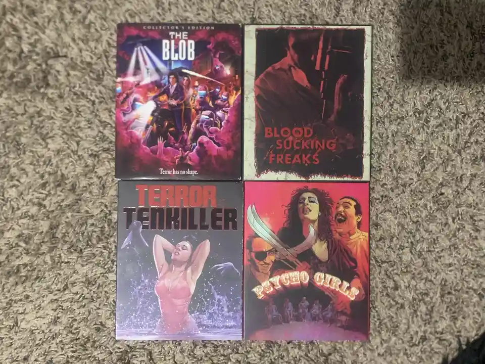 Four vintage-style horror movie covers are laid out on a carpeted floor. Top left shows 'The Blob' with a tagline 'Terror…