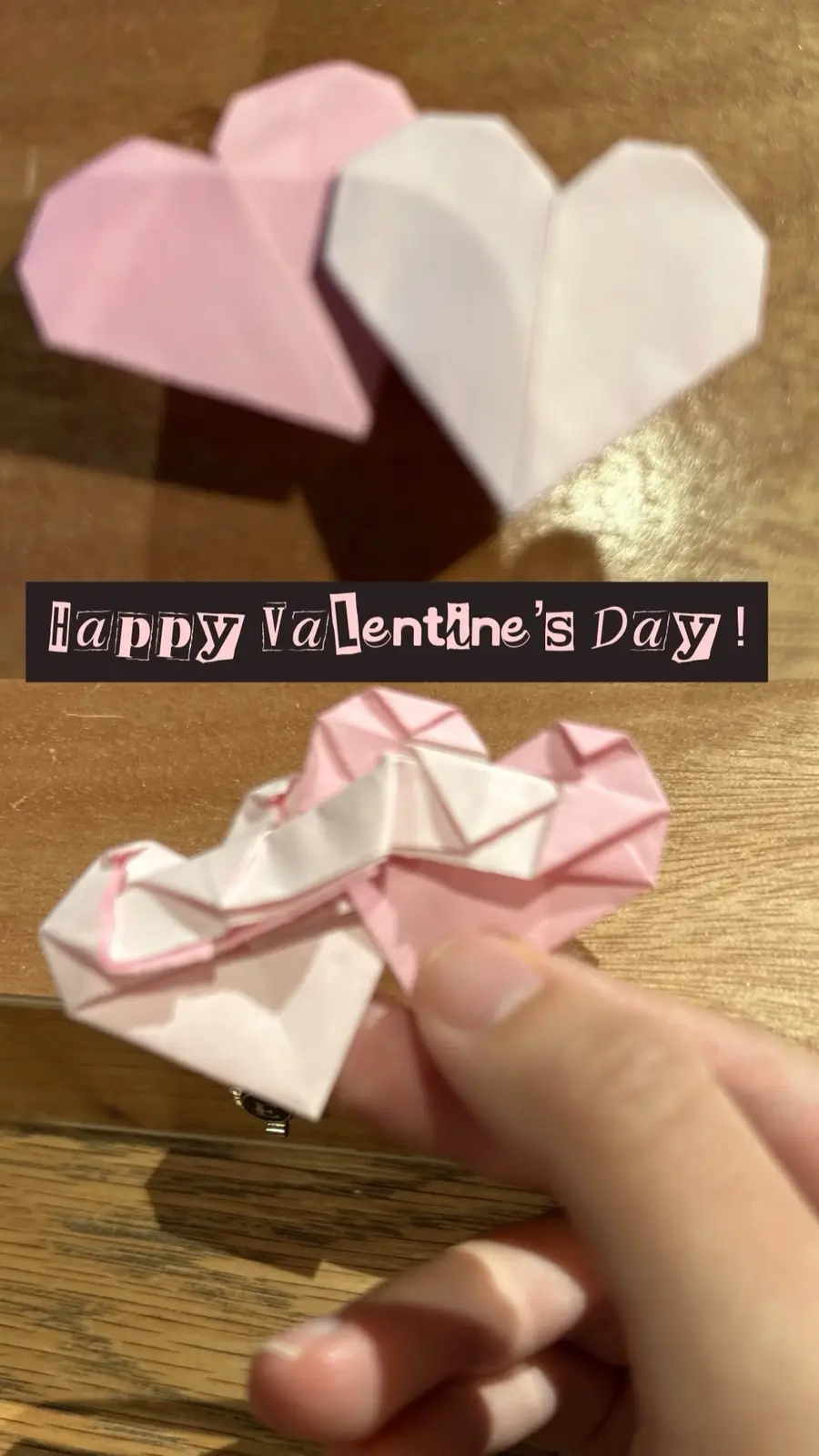The image shows two origami hearts, one pink and one white, placed on a wooden surface. A hand then holds the two hearts…