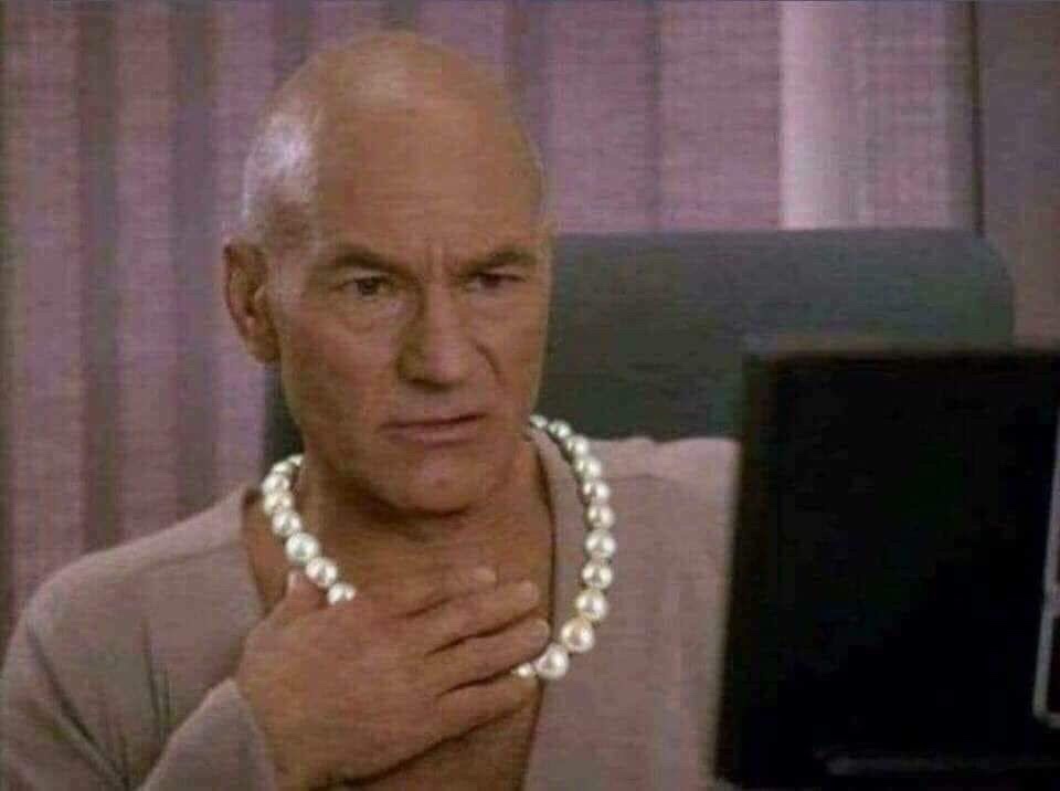 a still image of actor Patrick Stewart as Captain Picard from Star Trek, wearing a pearl necklace and placing his hand over…