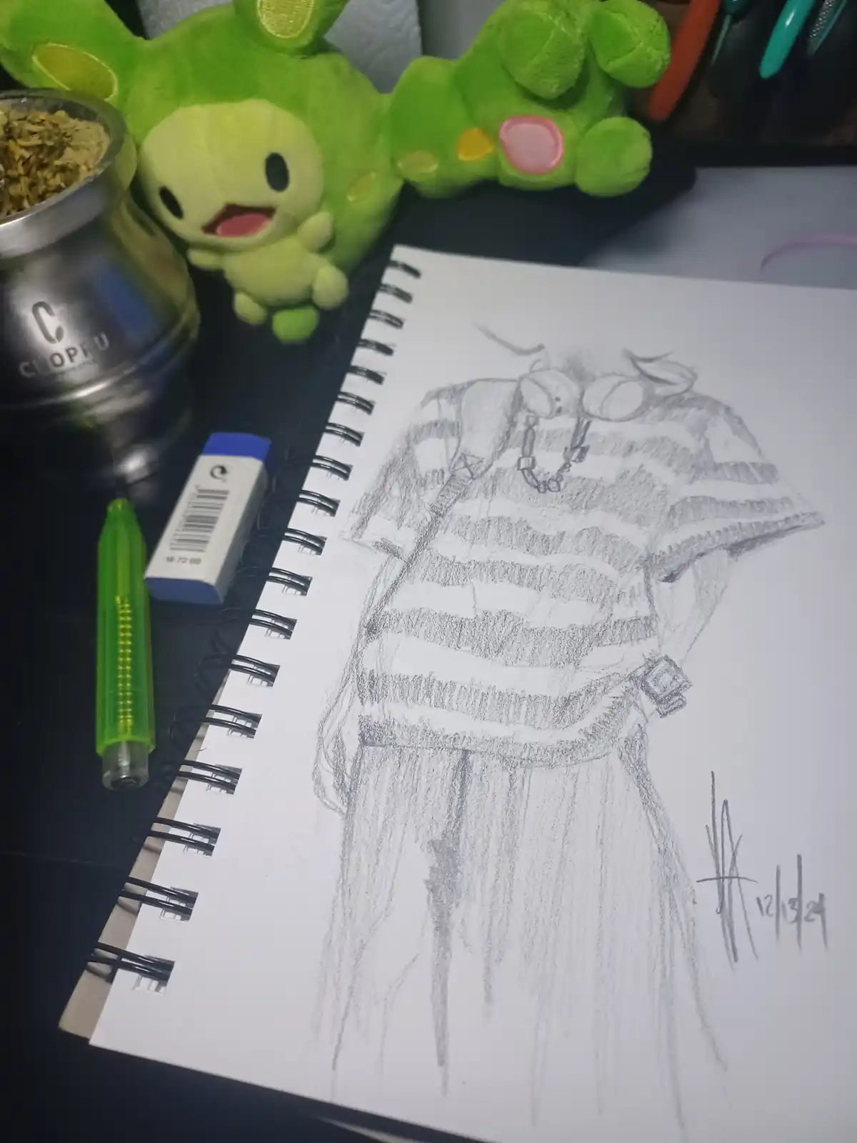 A pencil sketch in a spiral-bound notebook depicts a stylized, partially obscured figure wearing a striped shirt and…