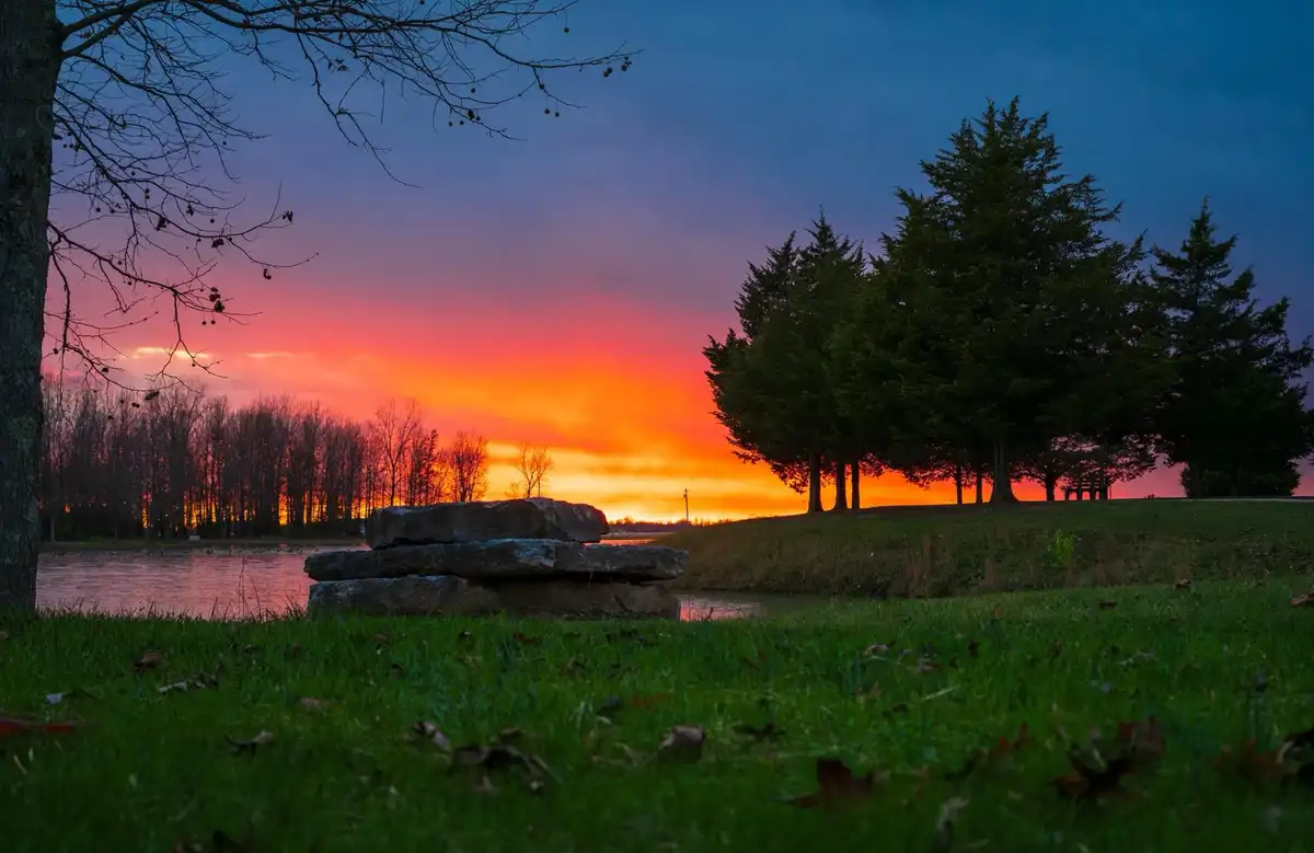 A serene landscape photo of a sunset over a lake with trees and grass, overlaid with the text 'i'm not lazy, i'm in…