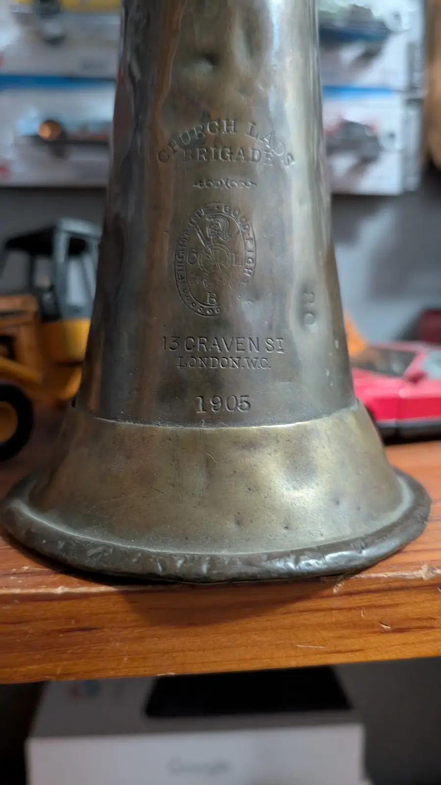 A close-up of a vintage brass fire alarm bell engraved with 'CHURCH LADS BRIGADE', a crest, '13 CRAVEN ST LONDON.W.C.', and…