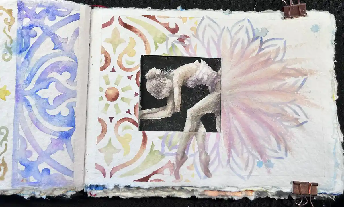An open handmade art journal with watercolor patterns on both pages, featuring a central black-and-white watercolor painting…