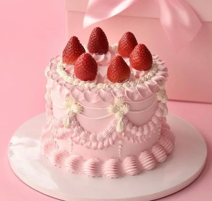 a beautifully decorated pink cake with white frosting, topped with fresh strawberries, sits on a white plate against a pink…