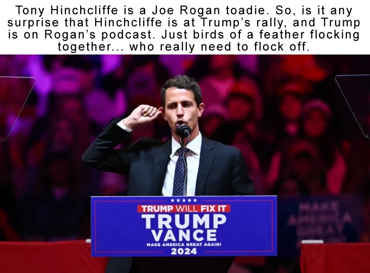 A man in a dark suit and tie stands at a podium with a blue sign reading 'TRUMP VANCE' and 'TRUMP WILL FIX IT' and 'MAKE…