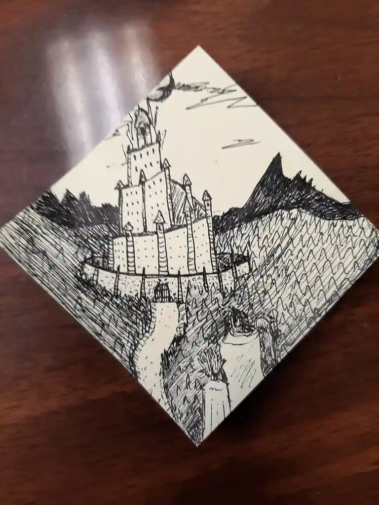 A hand-drawn black-and-white sketch on paper depicts a fantasy castle with multiple towers and turrets, surrounded by a moat…