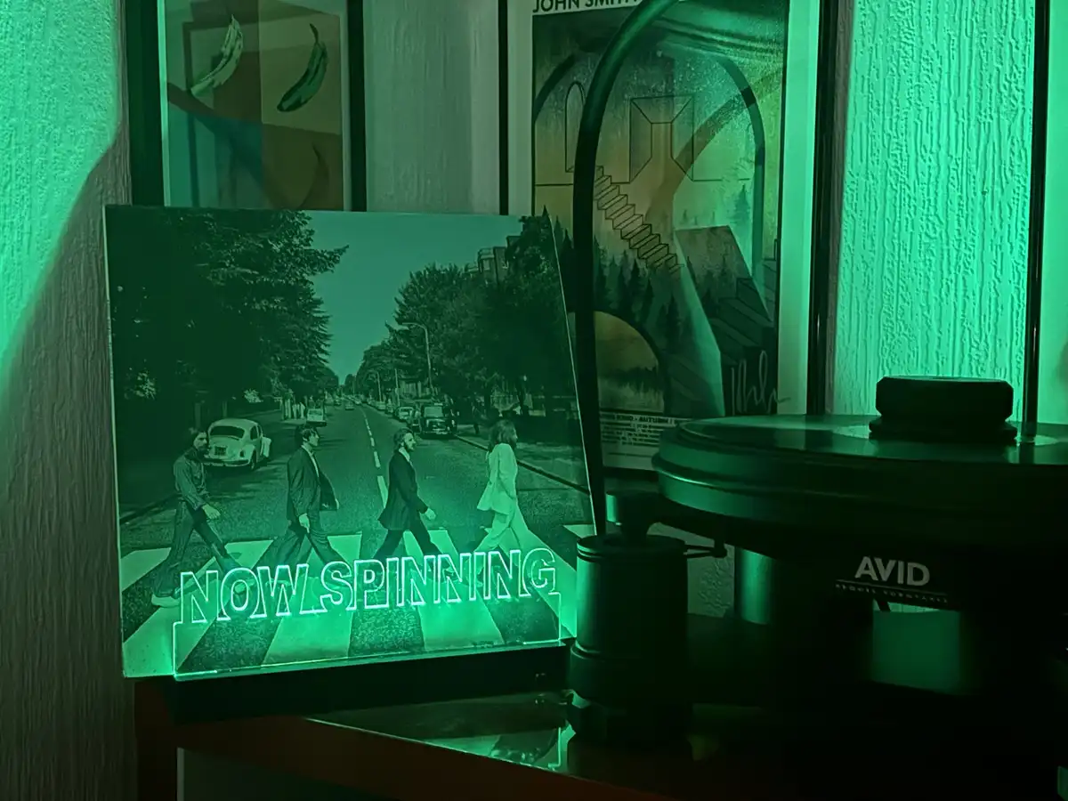 A green-tinted photo of The Beatles crossing a zebra crossing is displayed on a shelf next to a turntable. The image has…