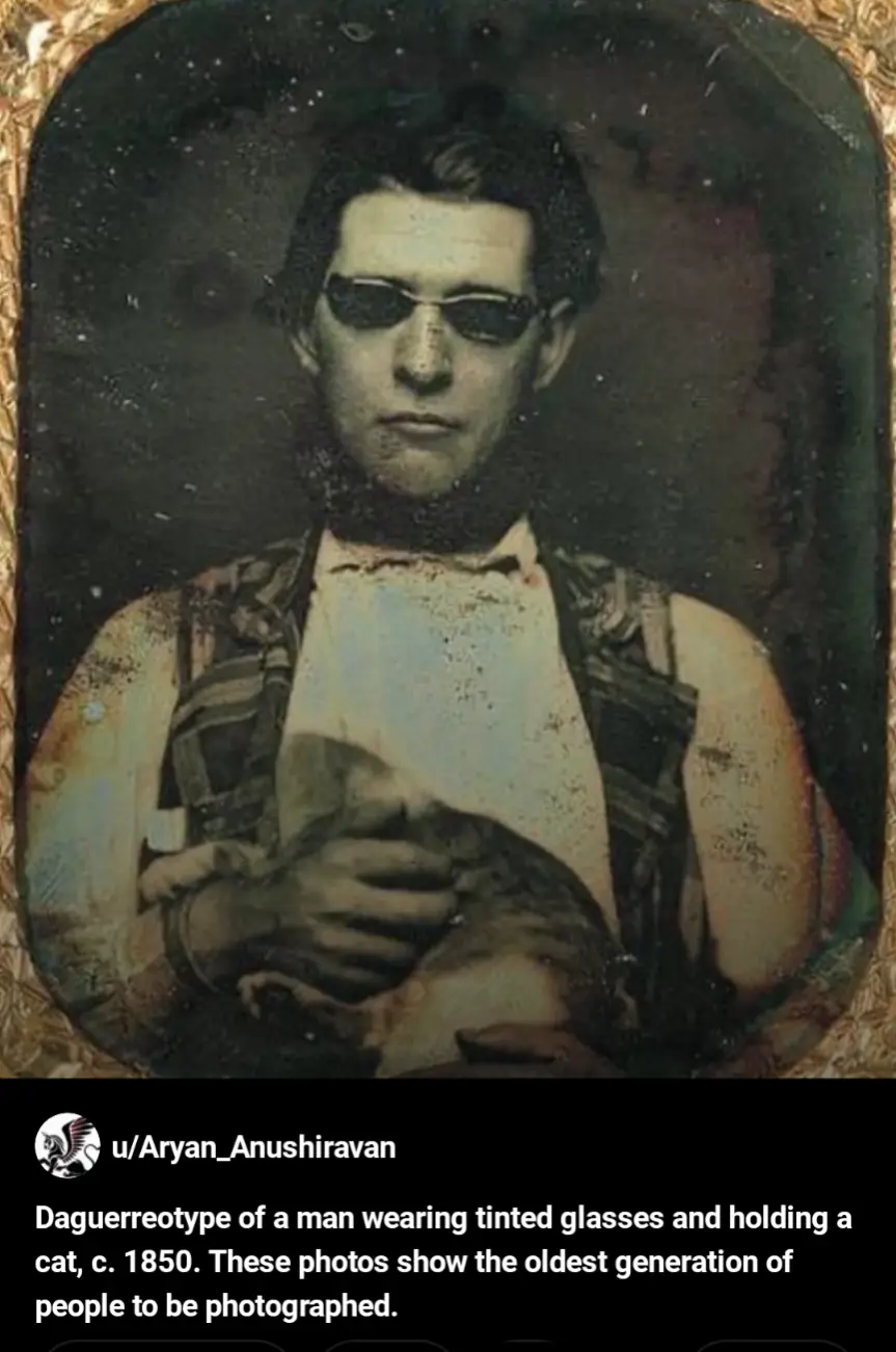 An old, grainy daguerreotype photo from around 1850 shows a man in period clothing holding a cat. He is wearing dark…