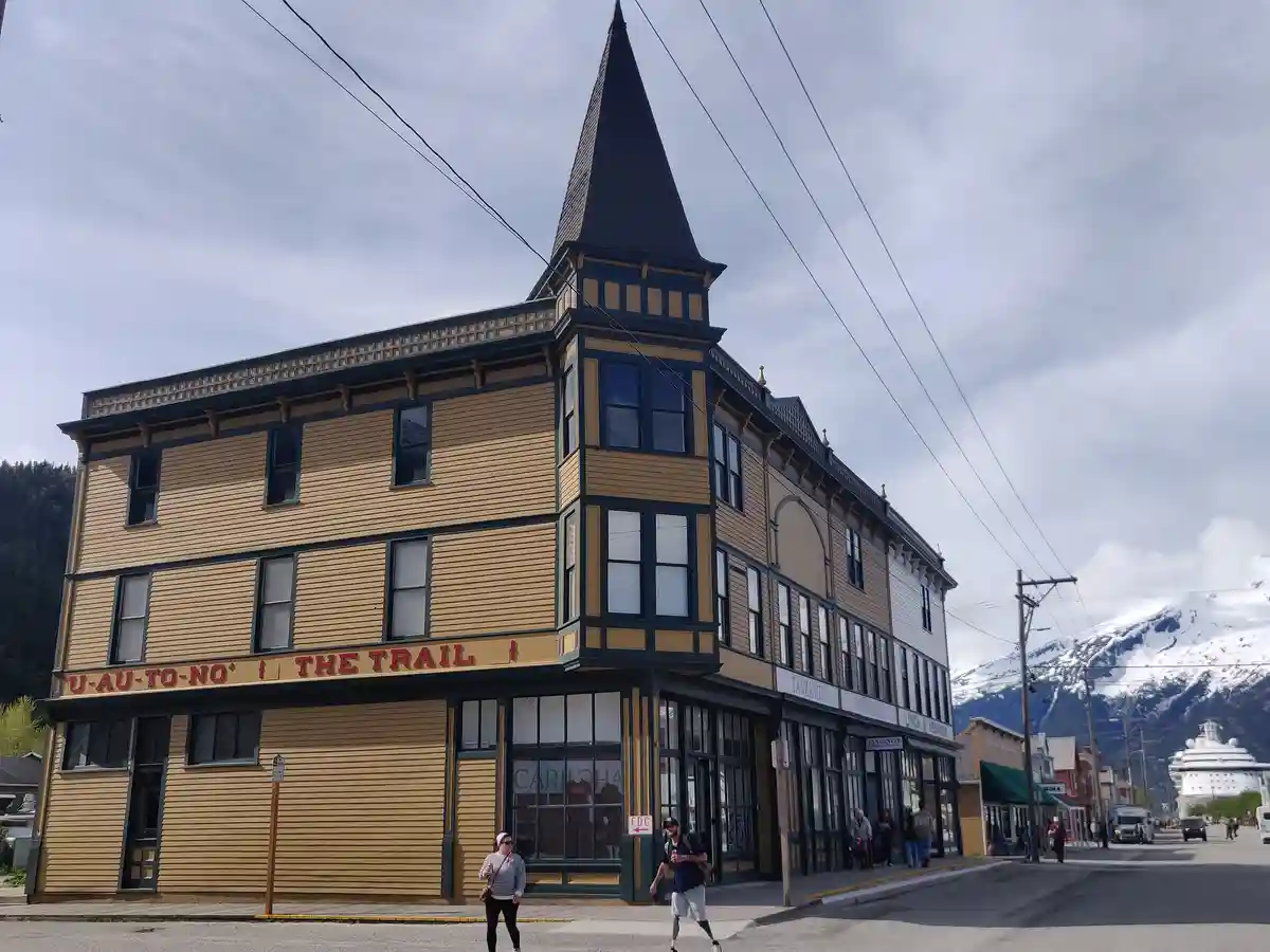 A photo of a yellow and dark green Victorian-style building with a pointed roof, featuring a red sign that reads…